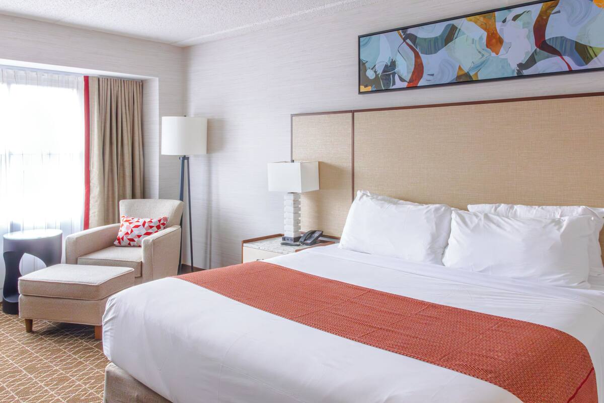 Une chambre d’hôtel avec un grand lit, une chaise, un bureau, une lampe et un tableau au mur.