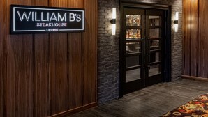 A wooden wall with a sign reading "William B's Steakhouse" and a glass door leading to the restaurant.