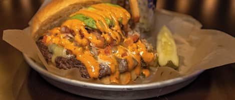 A burger with cheese, lettuce, and sauce, served with fries and a pickle on a metal tray.