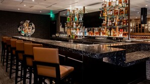 A bar area with a marble countertop, multiple liquor bottles, and bar stools.
