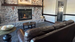 Une cheminée en pierre surmontée d’un tableau encadré, un canapé en cuir, une petite table et un ascenseur.