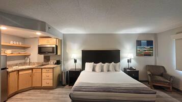 A hotel room with a bed, a desk, a chair, a microwave, a sink, and a painting on the wall.