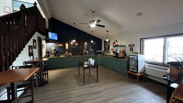A spacious restaurant with a high ceiling, a central island with a coffee machine, and a TV mounted on the wall.
