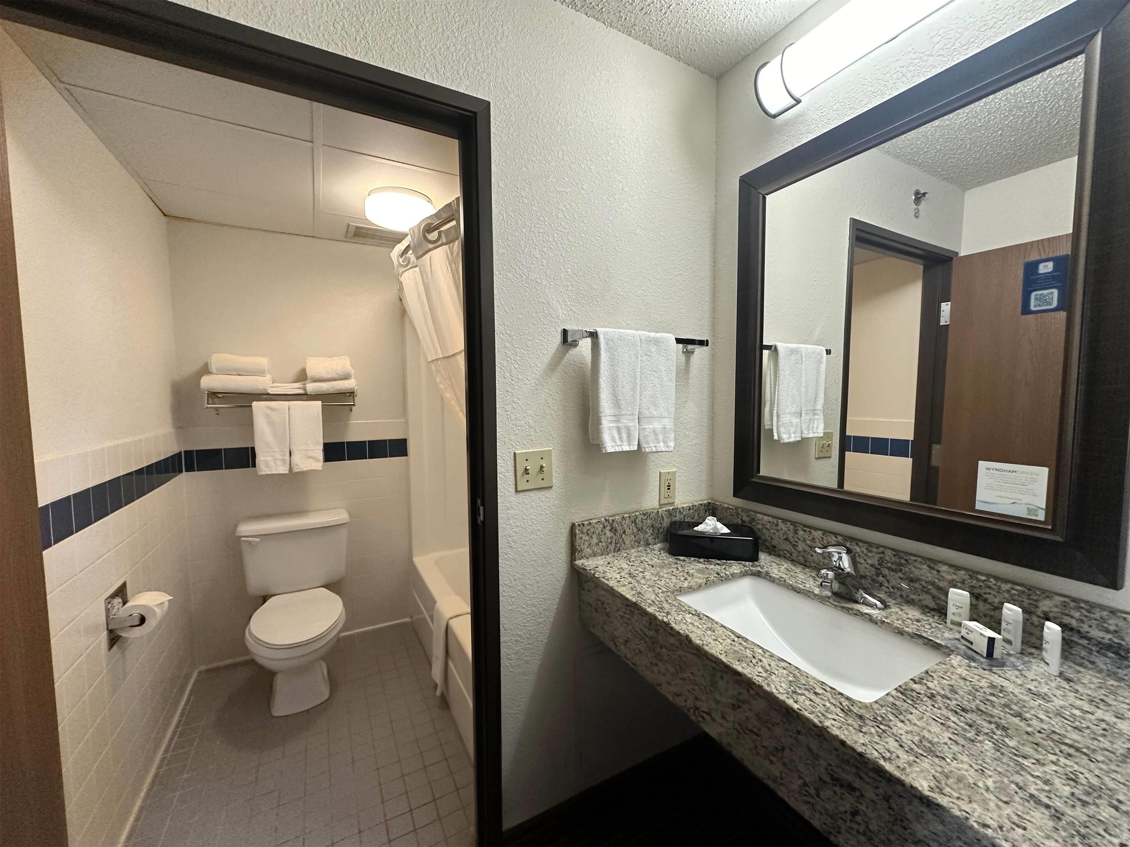 A bathroom with a toilet, sink, and mirror. There are towels on the wall and a tissue box on the counter.