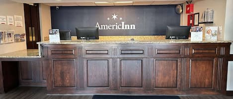 A reception desk with a dark wood finish, two computer monitors, and a sign reading "AmericInn by Wyndham".