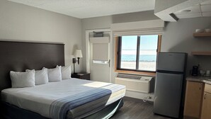 Une chambre d’hôtel équipée d’un lit, d’un bureau, d’un réfrigérateur, d’une fenêtre donnant sur la plage et d’une kitchenette.