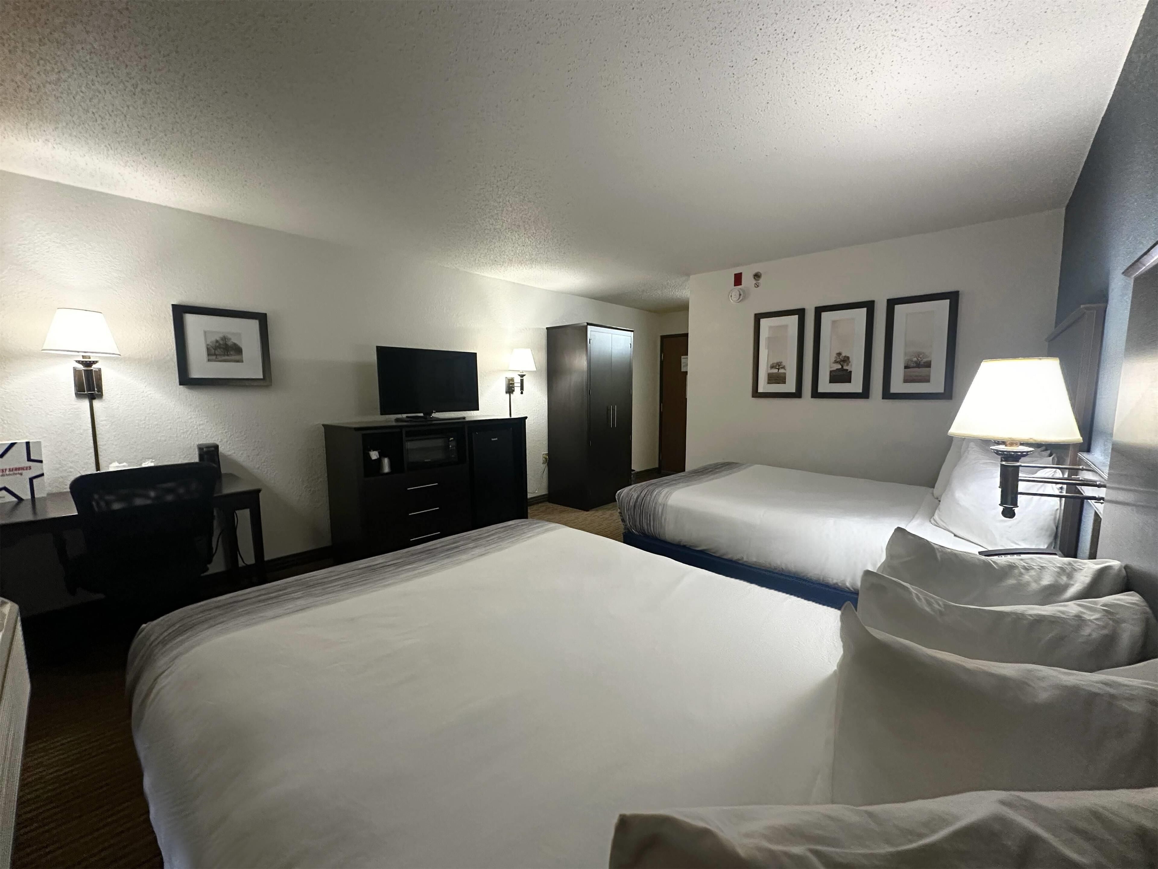Quarto de hotel com duas camas, uma escrivaninha com computador, televisão e armário.