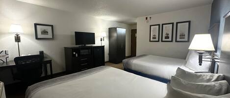 Habitación de hotel con dos camas, un escritorio con computadora, televisor y armario.