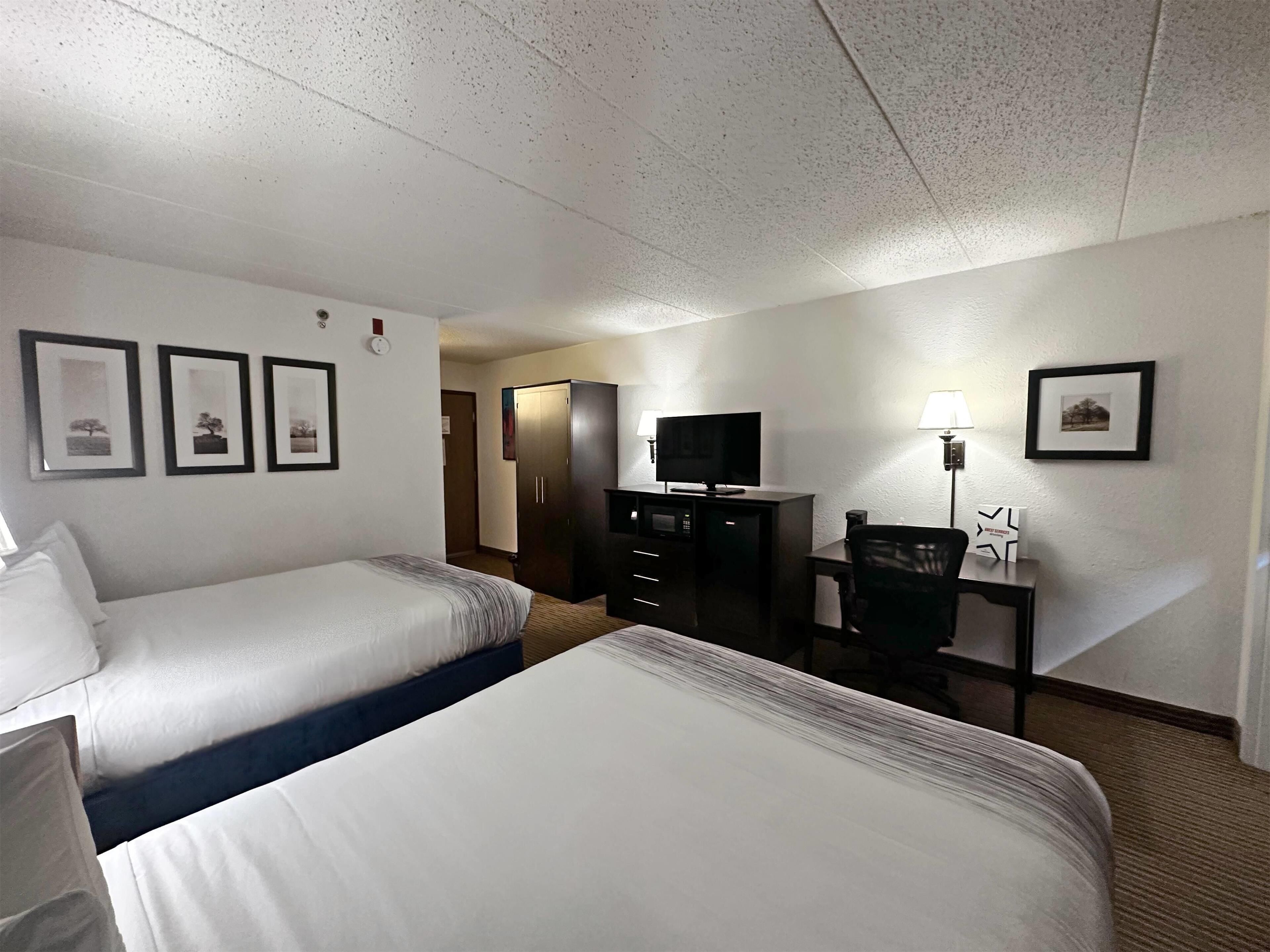 A hotel room with two beds, a desk with a lamp, a TV, and a wardrobe.