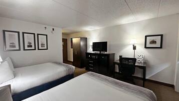 A hotel room with two beds, a desk with a lamp, a TV, and a wardrobe.