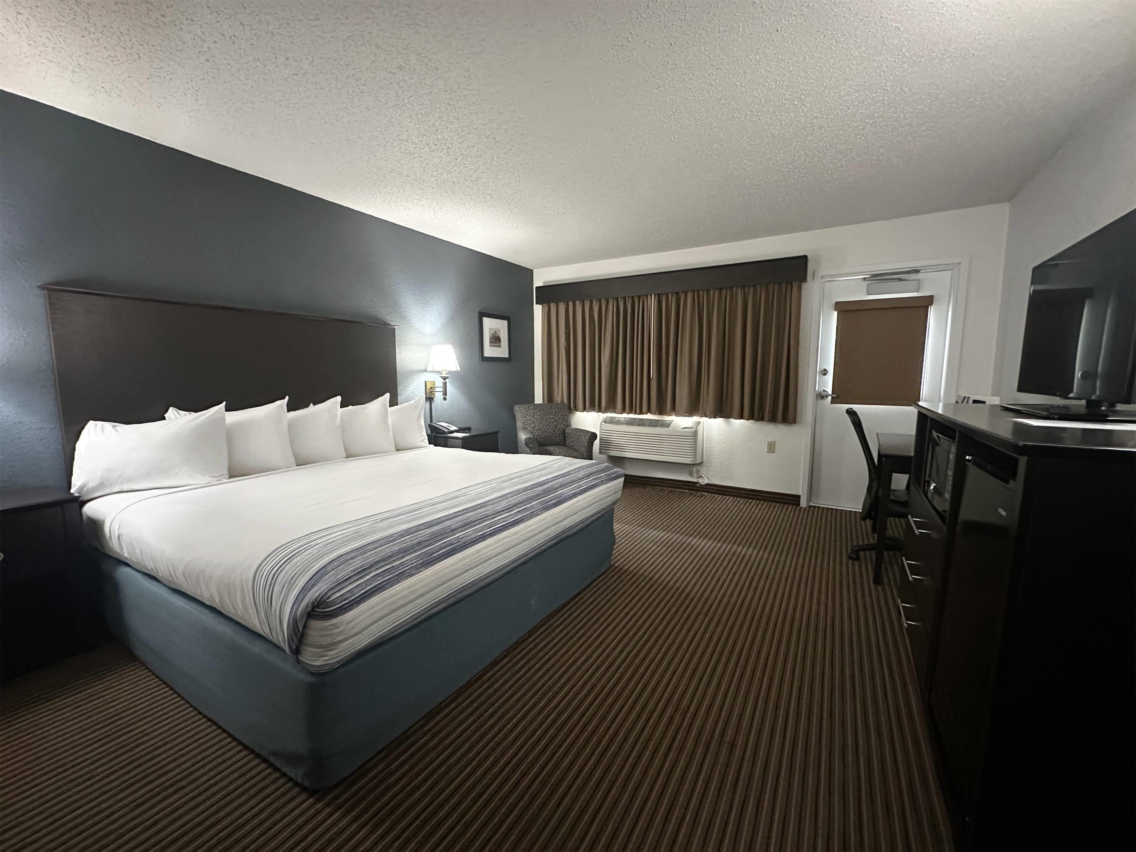 A hotel room with a large bed, a desk, a chair, a television, and a window with curtains.
