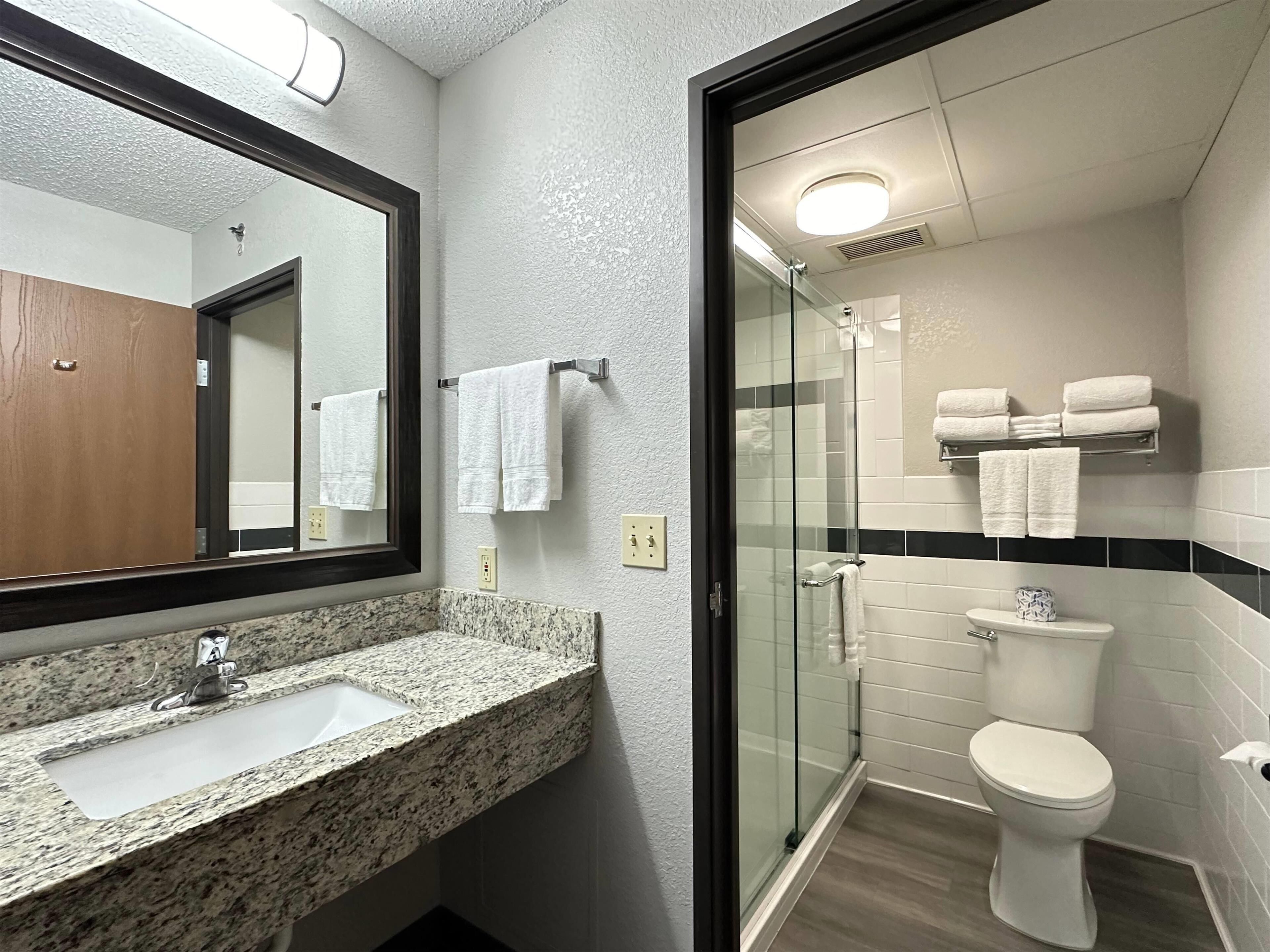 Un baño con lavamanos de encimera de granito, cabina de ducha con paredes de vidrio y inodoro blanco.