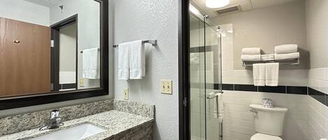 Un baño con lavamanos de encimera de granito, cabina de ducha con paredes de vidrio y inodoro blanco.