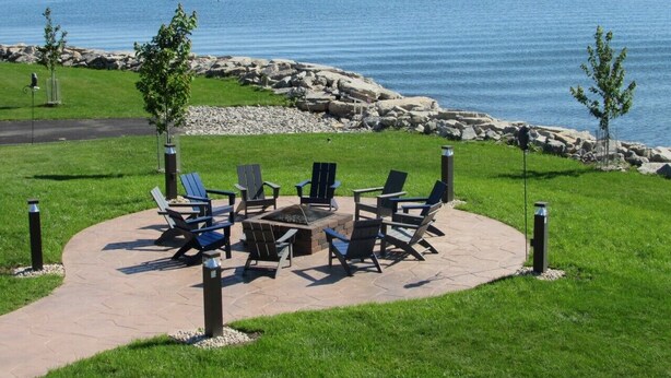Une terrasse avec des sièges extérieurs et un foyer, donnant sur une étendue d’eau.