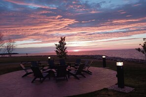 An outdoor seating area with chairs and tables, a small tree, and a view of the sunset over the water. - AmericInn by Wyndham Menominee (Menominee)