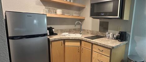 A compact kitchen with a stainless steel refrigerator, wooden cabinets, a microwave, and a granite countertop.