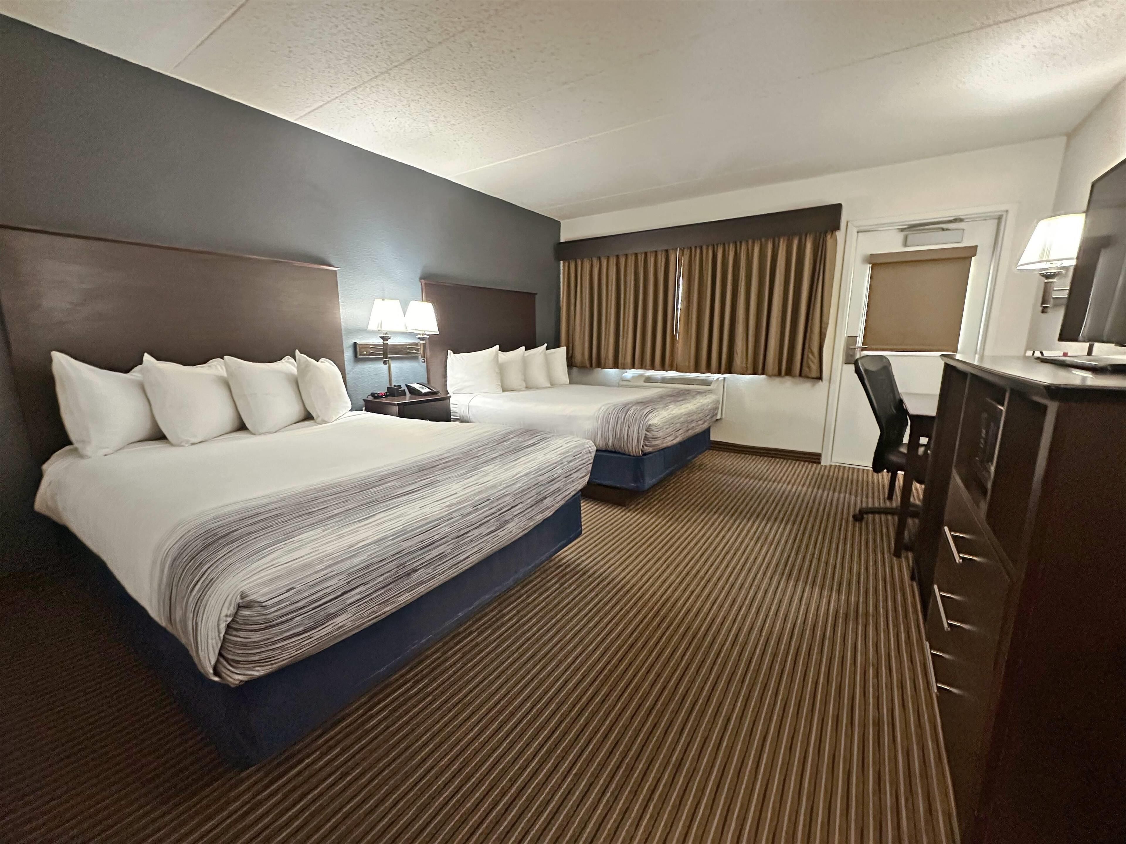 A hotel room with two beds, a desk, a chair, and a television.
