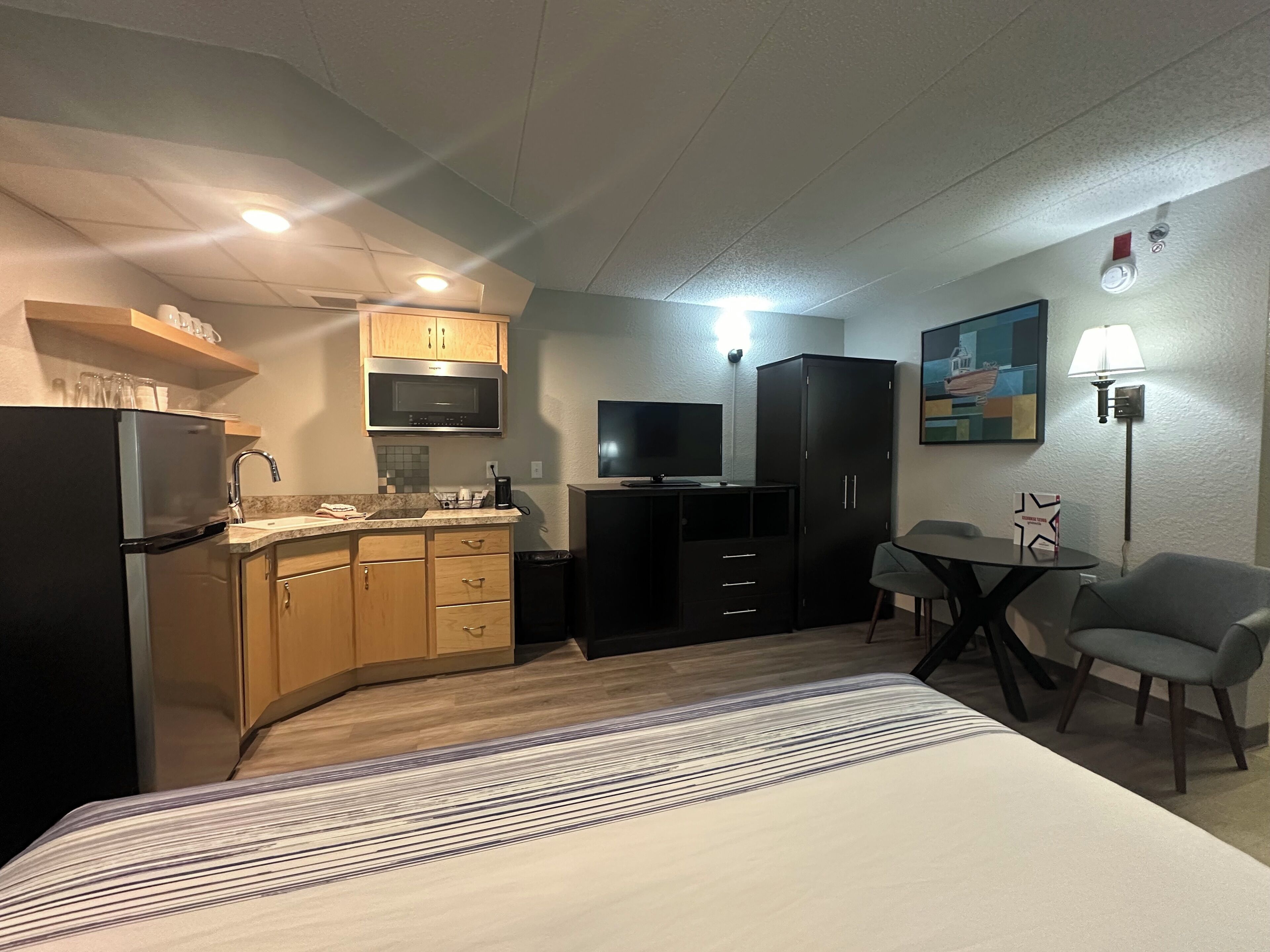 A compact hotel room with a bed, kitchenette, and a small dining area.