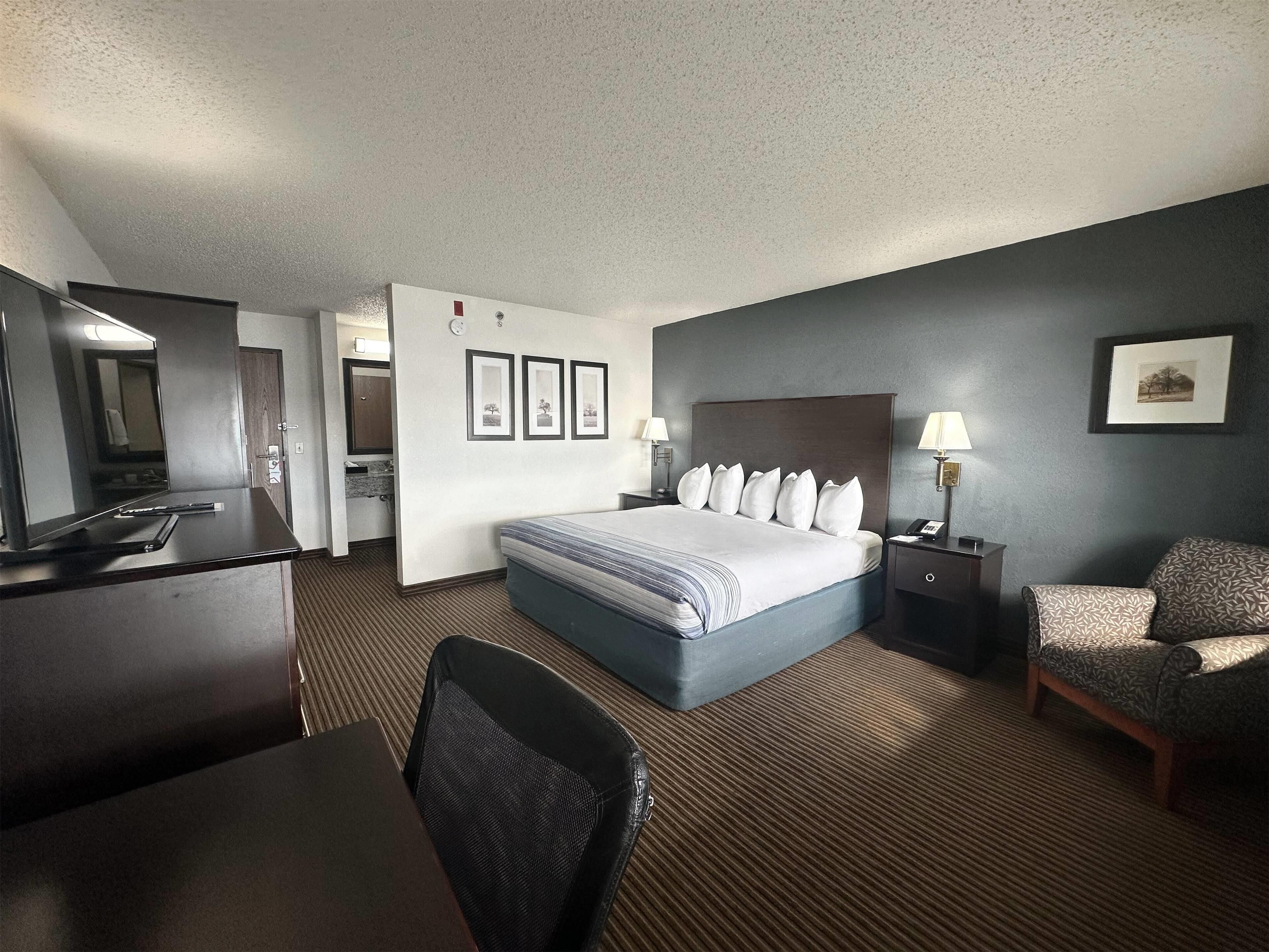 Een hotelkamer met een groot bed, een bureau, een stoel, een televisie en een badkamer zichtbaar door een geopende deur.