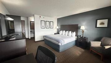Habitación de hotel con una cama grande, un escritorio, una silla, un televisor y un baño visible a través de una puerta abierta.