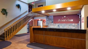 A reception desk with an American Inn logo, a wooden staircase, and a stone wall. - AmericInn by Wyndham Fargo West Acres (Fargo)