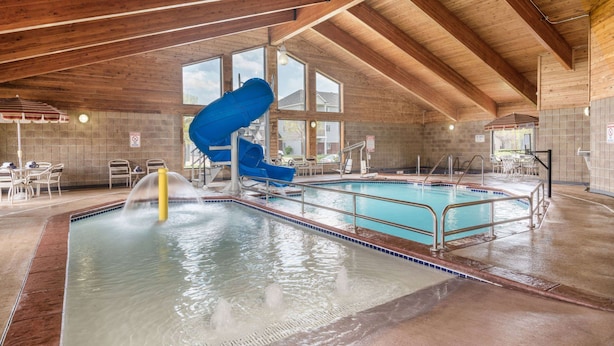 An indoor swimming pool with a blue slide, wooden beams, and large windows. - AmericInn by Wyndham Fargo West Acres (Fargo)