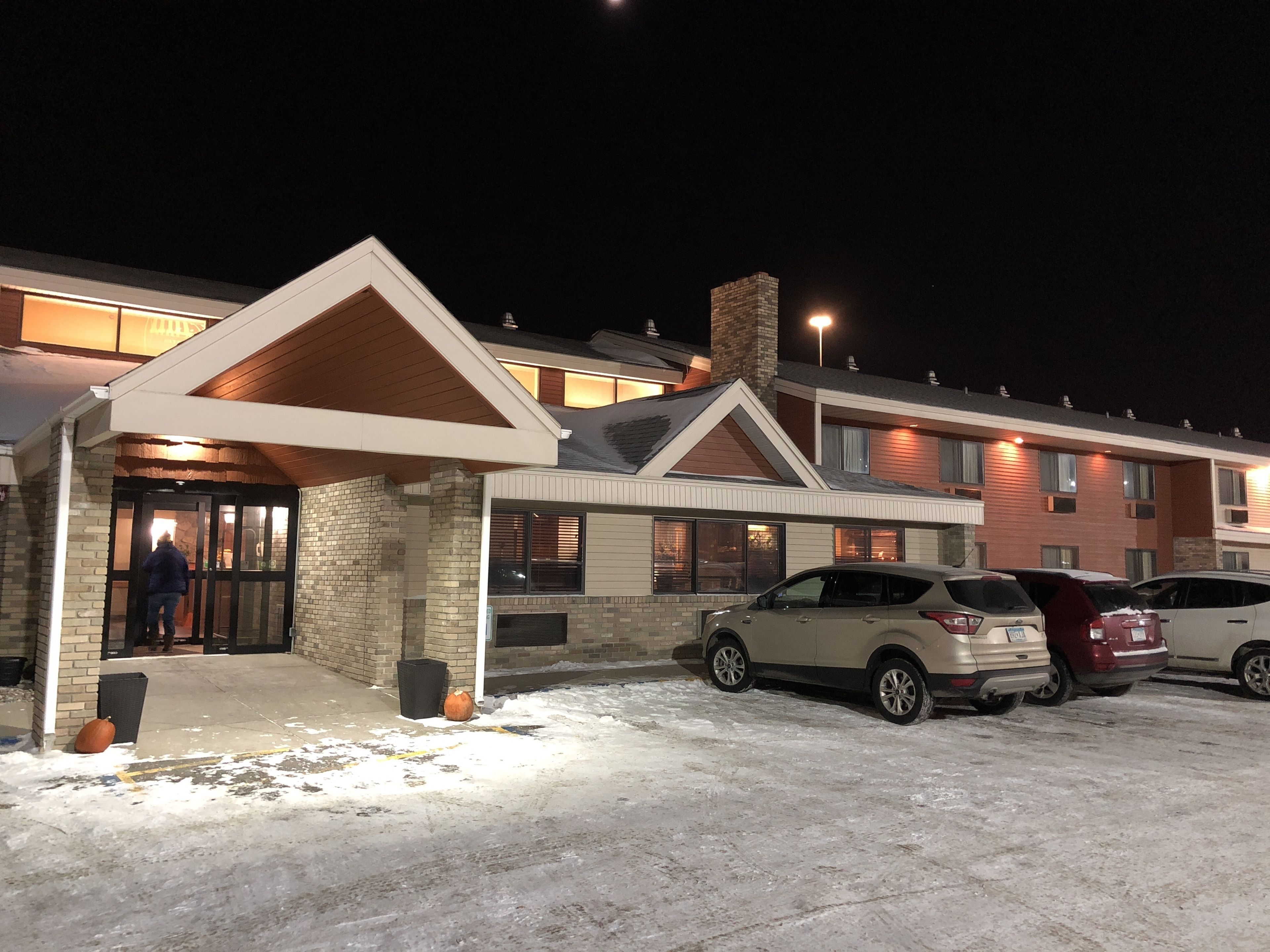 Un hôtel doté d’une entrée couverte, d’un parking avec des voitures et d’un sol recouvert de neige.