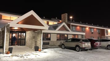 Un hôtel doté d’une entrée couverte, d’un parking avec des voitures et d’un sol recouvert de neige.