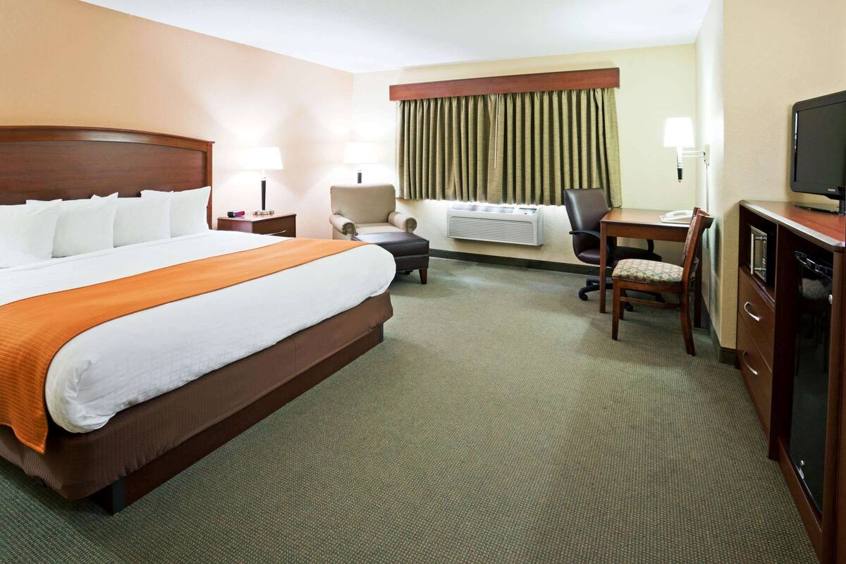 Una habitación de hotel con una cama grande, un escritorio, una silla, un televisor y una ventana con cortinas.