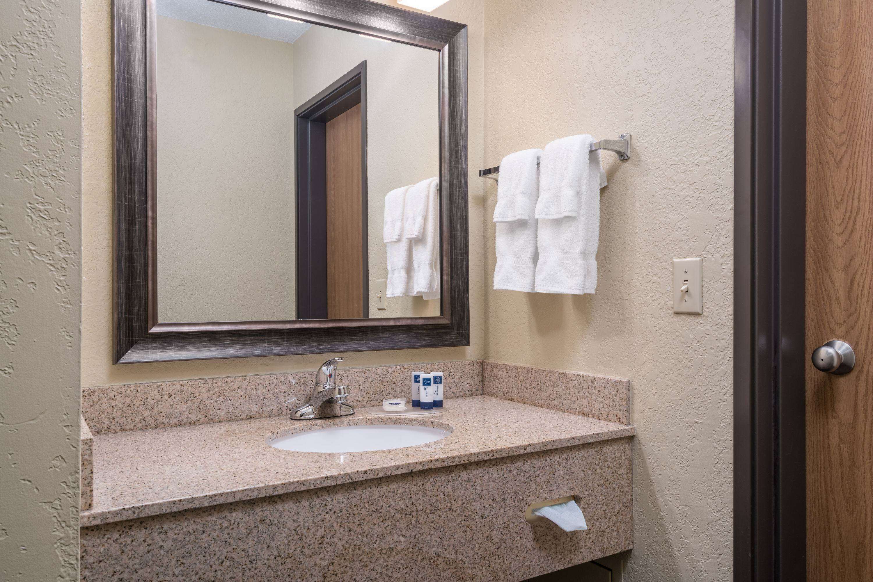 A bathroom with a granite countertop sink, a mirror, and a towel rack.