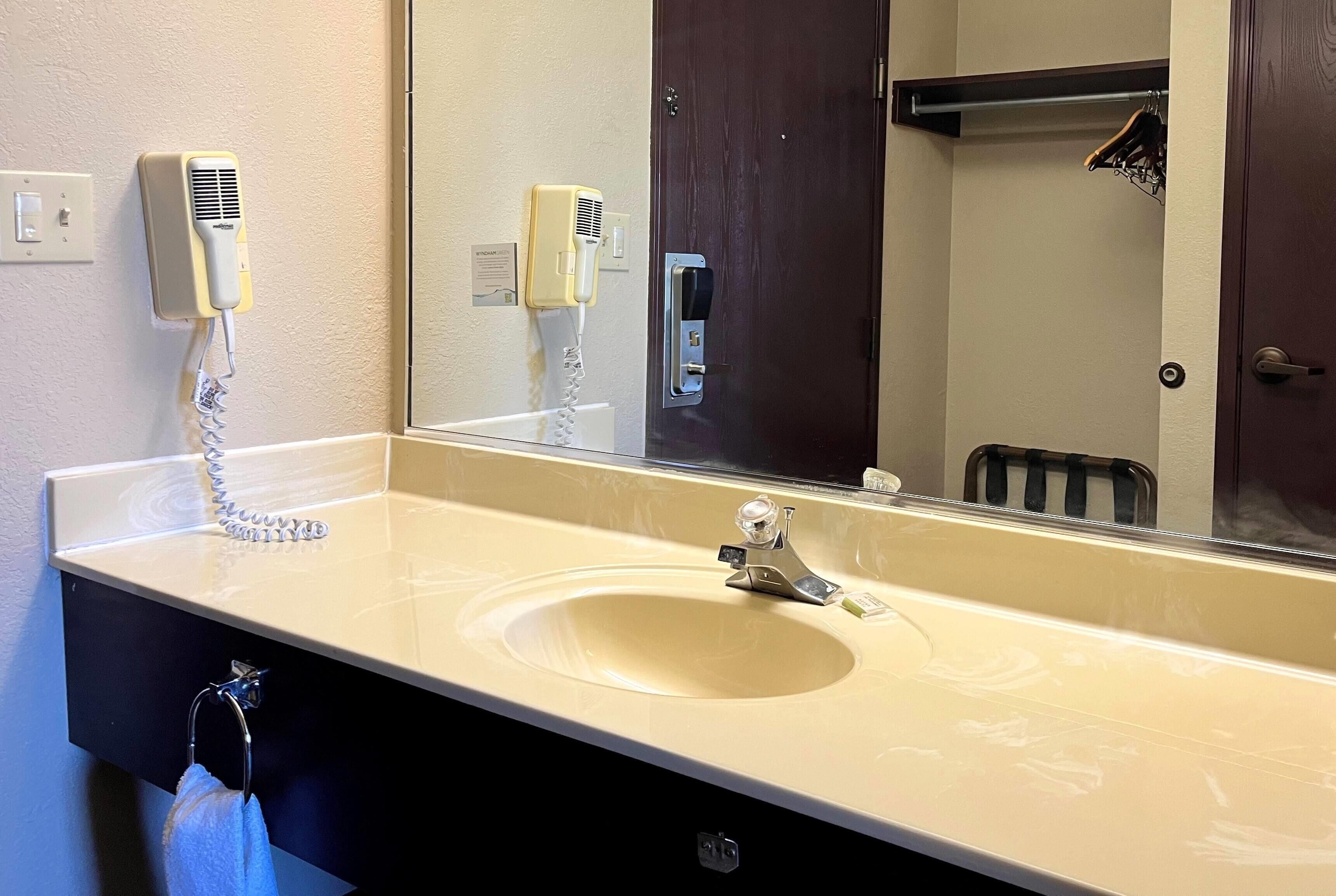 Un baño de hotel con lavamanos, espejo, secador de pelo y toallero.