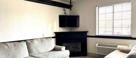 A living room with a fireplace, a flat-screen TV mounted above it, and a window with blinds.