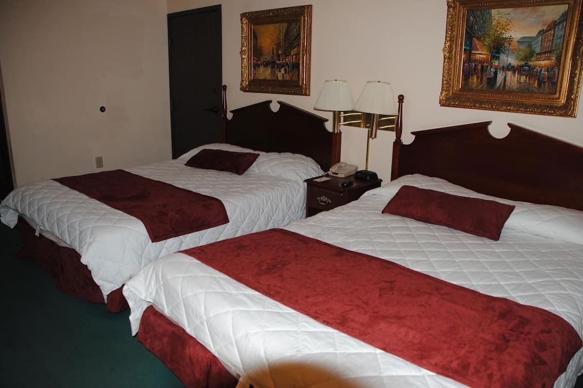 A hotel room with two beds, a nightstand, a lamp, and two paintings on the wall.