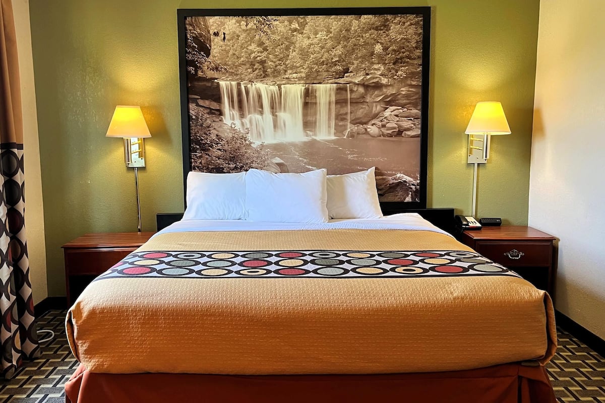 A hotel room with a bed, two bedside lamps, a large framed picture of a waterfall, and a patterned bedspread.