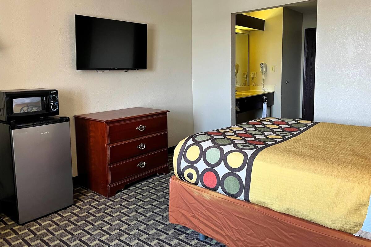 A hotel room with a bed, a dresser, a microwave, and a television.