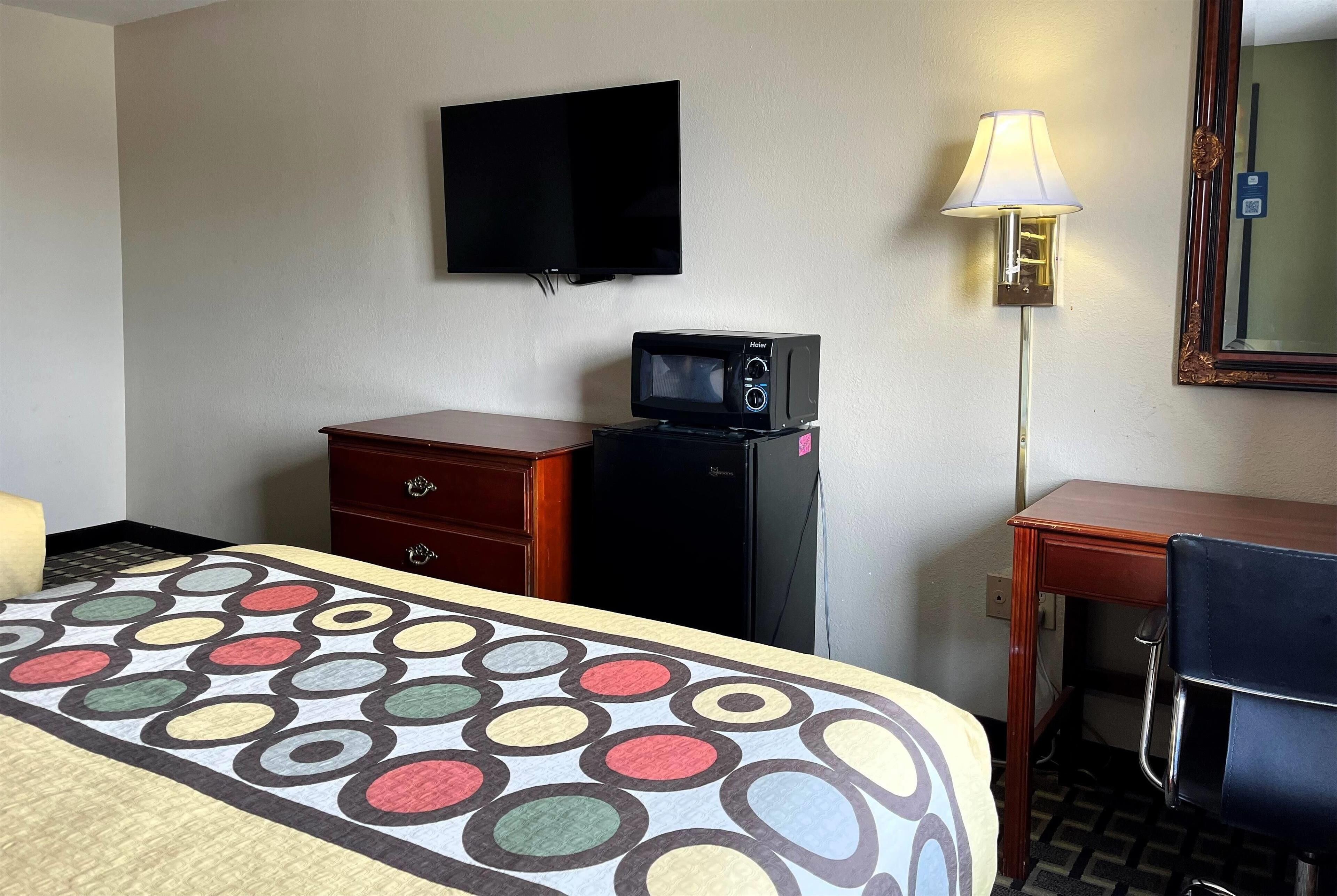 A hotel room with a bed, a desk, a television, a microwave, and a lamp.