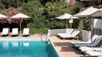 A swimming pool with lounge chairs and umbrellas, surrounded by greenery and trees.