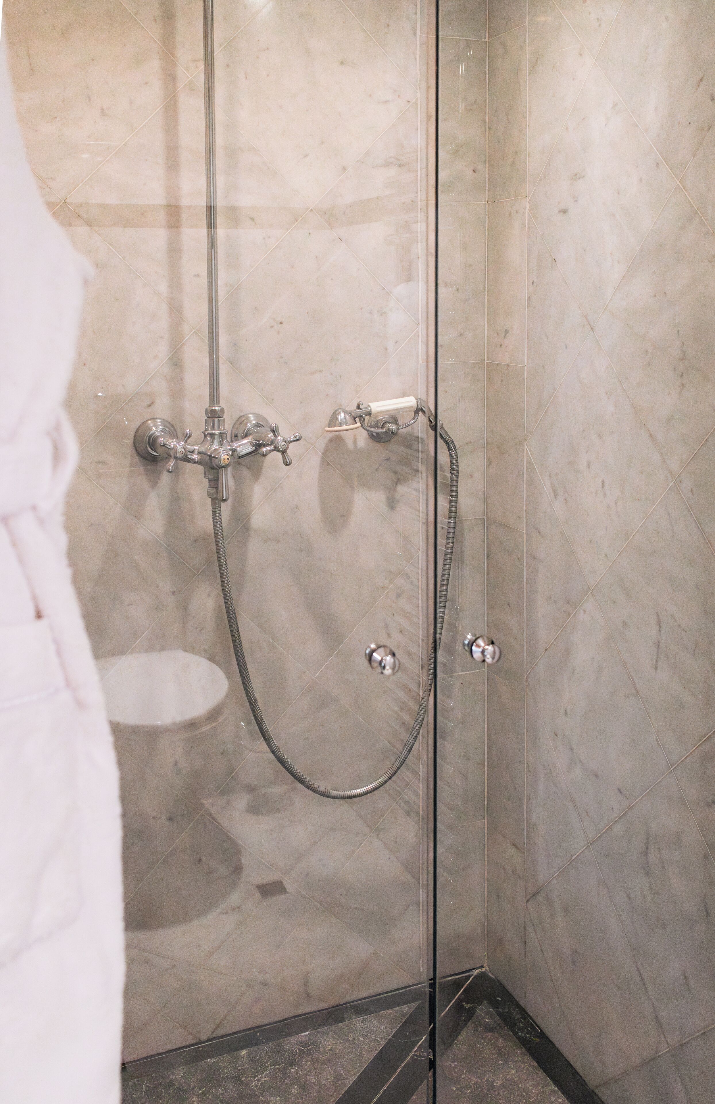 A glass-enclosed shower with a handheld showerhead and a wall-mounted faucet.