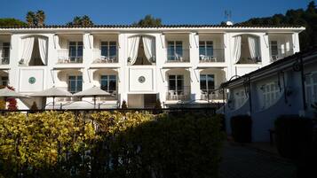A white building with multiple balconies, outdoor seating, and a clear blue sky.