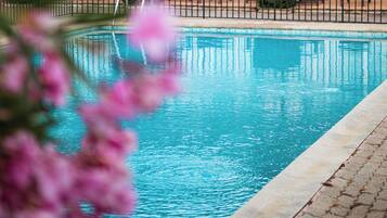 A swimming pool with a tiled deck, surrounded by a white building with a tiled roof, and a mountainous backdrop.