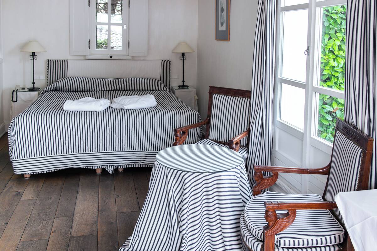 Ein Zimmer mit zwei Betten, einem runden Tisch und einem Stuhl, alles mit gestreifter Bettwäsche.