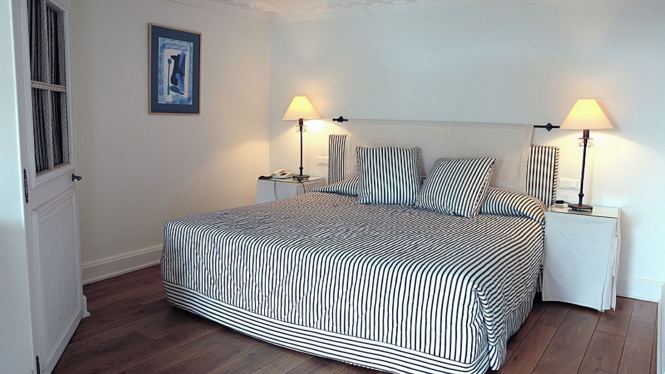A bedroom with a striped bedspread, two bedside lamps, a nightstand, and a framed picture on the wall.