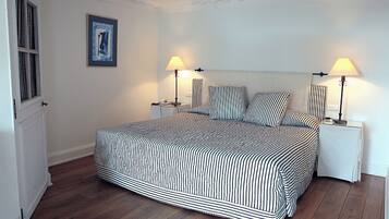 A bedroom with a striped bedspread, two bedside lamps, a nightstand, and a framed picture on the wall.
