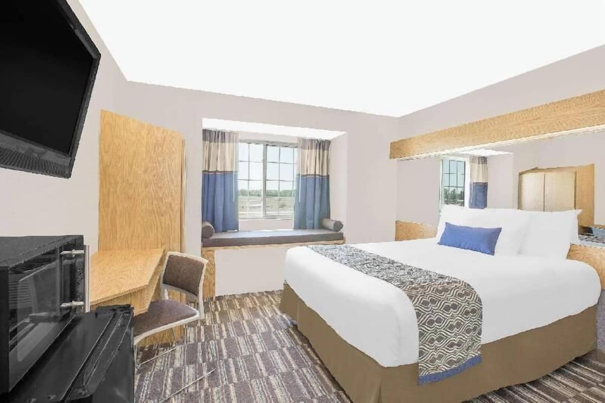 A hotel room with a bed, a desk, a television, a window with curtains, and a view of the outdoors.