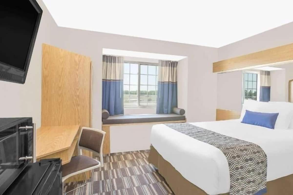 A hotel room with a bed, a desk, a TV, and a window with curtains.