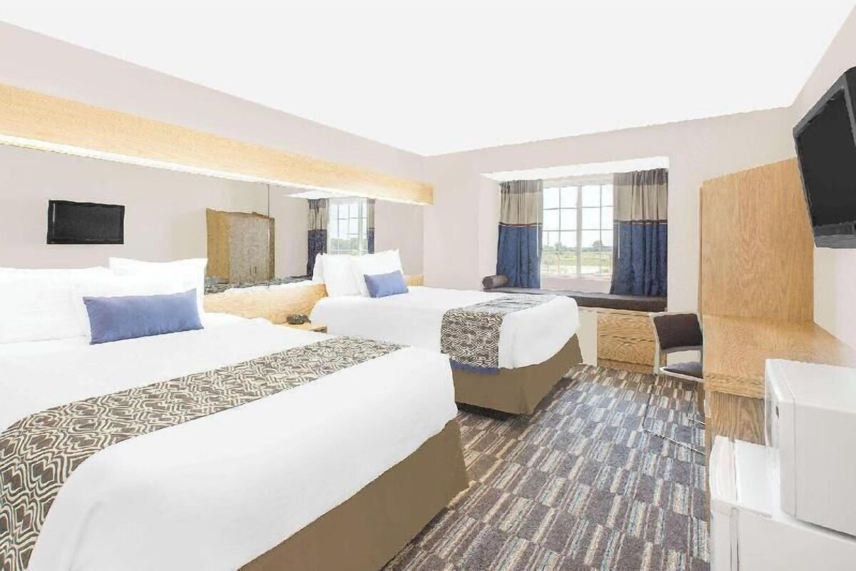 A hotel room with two beds, a desk, a chair, a TV, and a window with curtains.