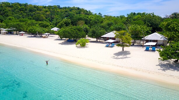 Una playa con agua turquesa cristalina, arena blanca y varias cabañas de playa con sombrillas.