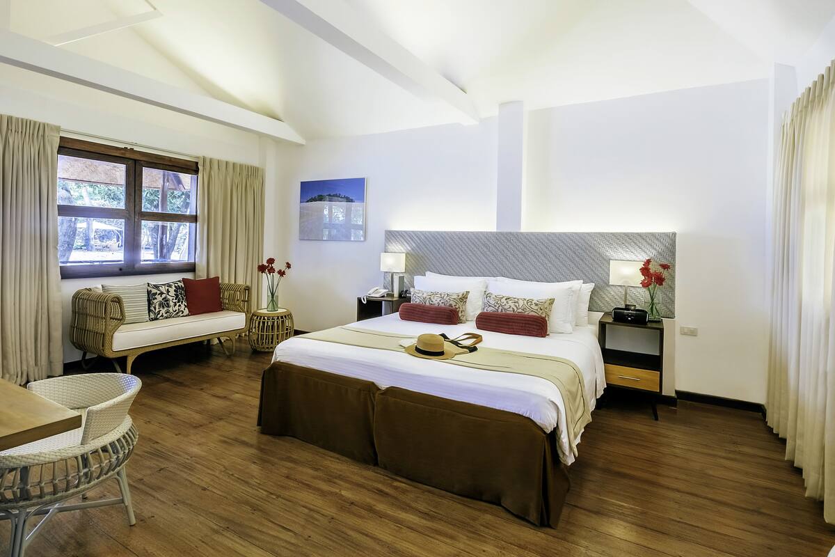 Quarto de hotel com uma cama grande, um sofá, uma mesa de jantar e uma janela com cortinas.