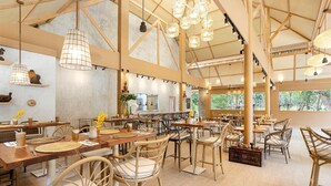 Un restaurante espacioso con techos altos, vigas de madera a la vista y mobiliario de mimbre. Las mesas están preparadas con manteles individuales y centros de mesa.