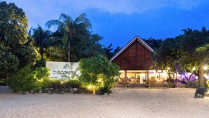 Un resort con un edificio de madera, rodeado de abundante vegetación y palmeras, con un letrero que dice "DISCOVER CORON".